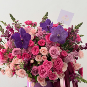 Arreglo en base lila con orquídeas vanda moradas y rosas en tonos rosa y fucsia